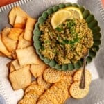 Olive tapenade in a bowl garnished with lemon wedges and with crackers.
