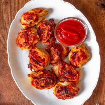 A platter of pizza rolls with marinara sauce on a wood surface.