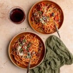 Two bowls of pasta next to a glass of wine.