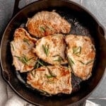 Pork loin steaks in a skillet topped with rosemary.