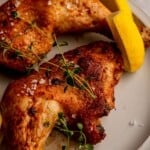Roasted chicken leg quarters with lemon wedges.