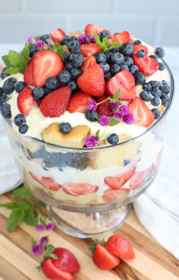 Glass trifle bowl layered with yellow cake whipped cream and strawberries and blueberries.