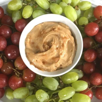 Brown sugar maple dip in a white bowl surrounded by green and red grapes.