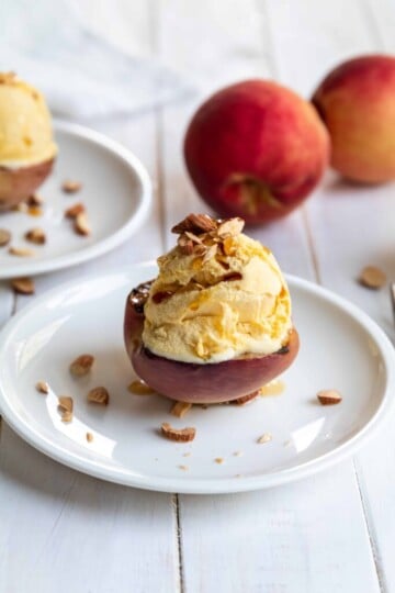 Peach half topped with peach ice cream scoop and almonds on a white plate.