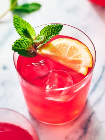 Pink drink in a glass with a lemon wedge and sprig of mint.