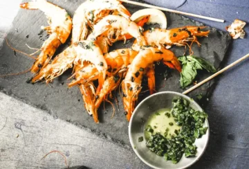 Whole unpeeled grilled shrimp on a black platter with basil marinade.