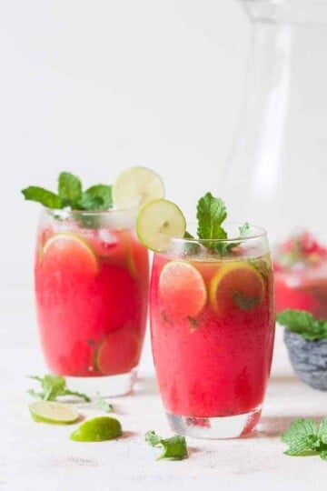 Two glasses of pink drinks with lime wheels and mint sprig garnish.