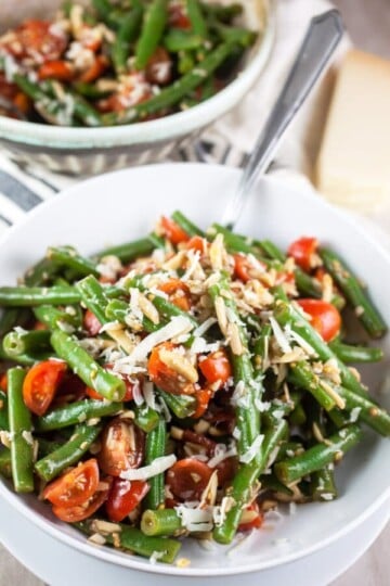 Green bean salad, tomatoes, slivered almonds, parmesan cheese in a white bowl.