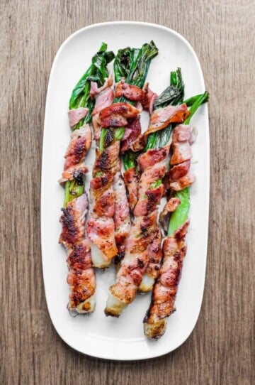 Spring onions wrapped in pancetta on a white platter.