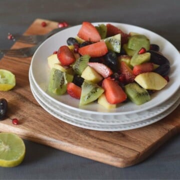 Strawberries, kiwi, apples and red grape salad on stacked white plates.