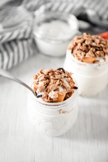 White cream in mason jar topped with peaches and granola.