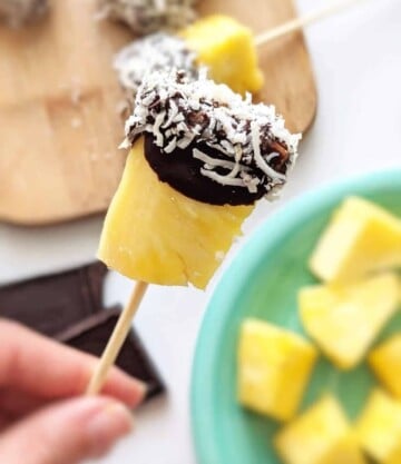 hand holding a toothpick with a chocolate covered pineapple slice and shaved coconut