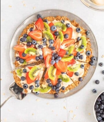 Metal pie knife grabbing a slice of fruit covered pizza.
