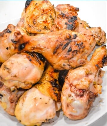 Stacked grilled chicken drumsticks on a white plate.