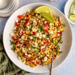 A bowl of corn and red pepper salad topped with lime wedges.