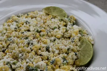 Grilled Mexican street corn, queso fresco, lime wedges in a white bowl.