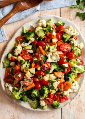 Marinated broccoli, cauliflower, zucchini, tomatoes and red bell pepper salad on a cream plate.