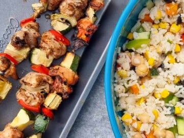 Chicken skewers with zucchini and red bell pepper next to a blue bowl of vegetables rice.