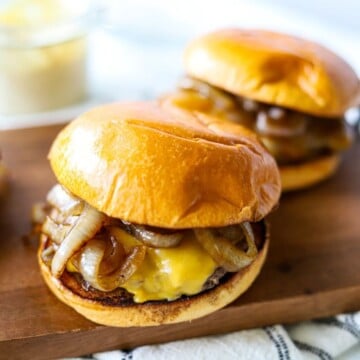 Two smashed burgers on buns with yellow cheese and sautéed onions on a wooden board.