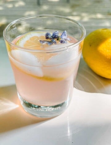 Light pink lemonade in a short glass with lemon and violets.