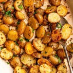 A spoon digging into roasted potatoes.