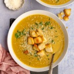 A white bowl of broccoli soup topped with toasted bread.
