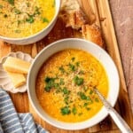 Bowls of pastina soup on a cutting board with bread.