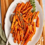 A white plate filled with roasted carrots garnished with sprigs of fresh thyme, placed on a wooden cutting board.