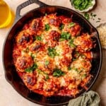 Meatballs in a cast iron skillet topped with mozzarella cheese and parsley.
