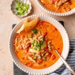 A table set with creamy chicken taco soup, topped with green onions and a side of tortilla chips.