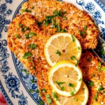 Parmesan-crusted chicken on a blue and white plate, garnished with lemon slices.