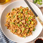 Bowl of chicken fried rice with chopsticks, accompanied by a small dish of soy sauce and a striped napkin.