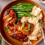 Air fryer teriyaki chicken thighs garnished with sliced green onions and served alongside white rice and green beans.