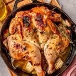 A close-up of a golden-brown spatchcock chicken in a cast-iron skillet.