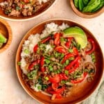 Thai basil beef over rice, garnished with green onions and fresh basil, with lime wedges and extra basil leaves nearby.