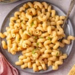 Three-cheese macaroni and cheese on a gray plate, garnished with fresh chives and black pepper.