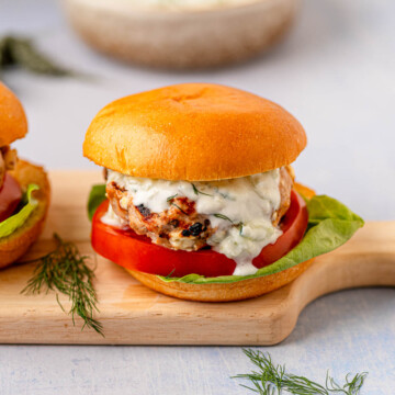 Side view of assembled Greek turkey burger on a wooden board with lettuce and tomato.