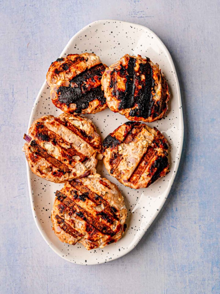 Platter of grilled Greek turkey burger patties with charred grill marks and flecks of onion and feta.