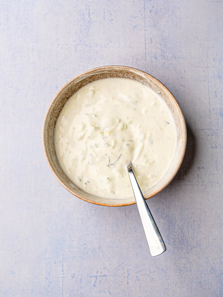 Creamy homemade tzatziki sauce with shredded cucumber and dill in a rustic bowl.