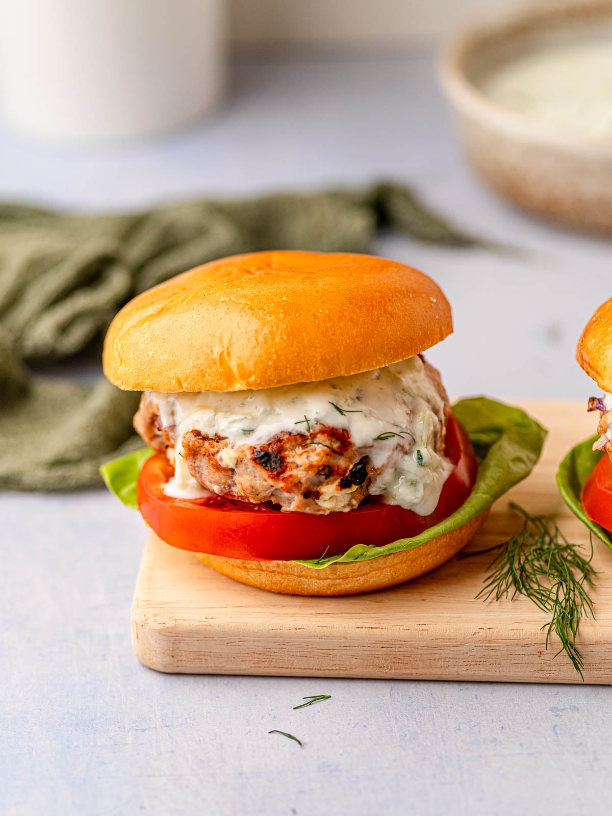 Greek turkey burger with lettuce, tomato, and tzatziki on a toasted bun garnished with fresh dill.