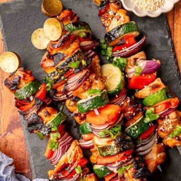 Grilled teriyaki chicken kabobs served on a slate board with sesame seeds.