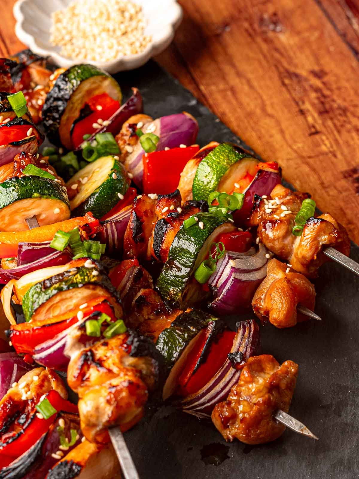 Charred teriyaki chicken skewers garnished with scallions and sesame seeds.