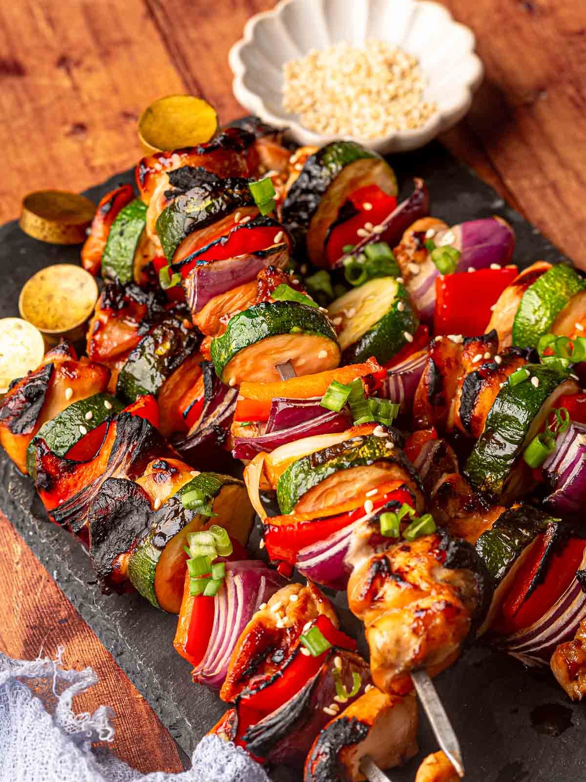 Colorful grilled chicken kabobs with veggies on a black serving platter.