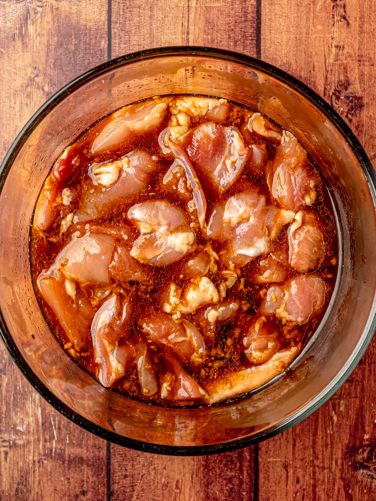 Chicken marinating in a homemade teriyaki sauce in a glass bowl.