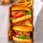 Two turkey burgers with fries in a parchment-lined tray, ready to serve.