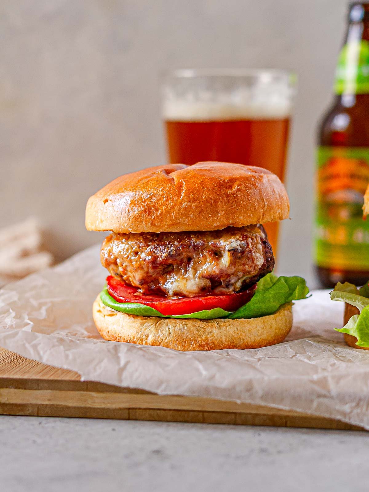 Juicy air fryer turkey burger on a brioche bun with lettuce and tomato, served on parchment paper with a glass of beer in the background.