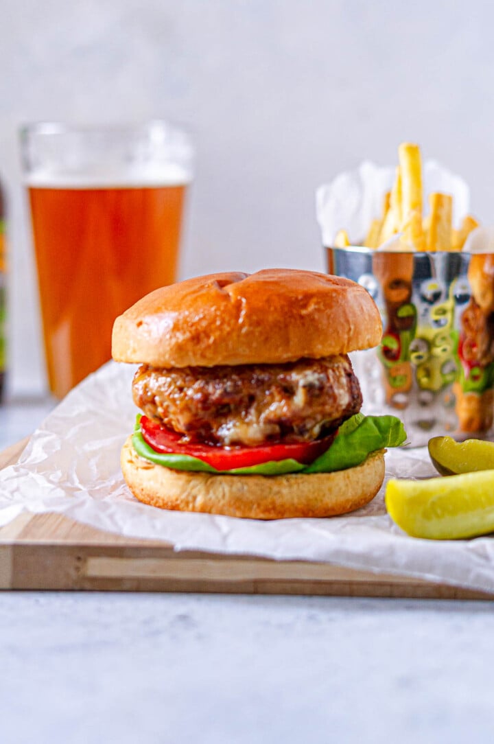 Air fryer turkey burger with tomato and lettuce on a bun, served with fries, pickles, and a pint of amber beer.