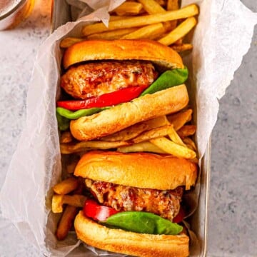Two turkey burgers with fries in a parchment-lined tray, ready to serve.