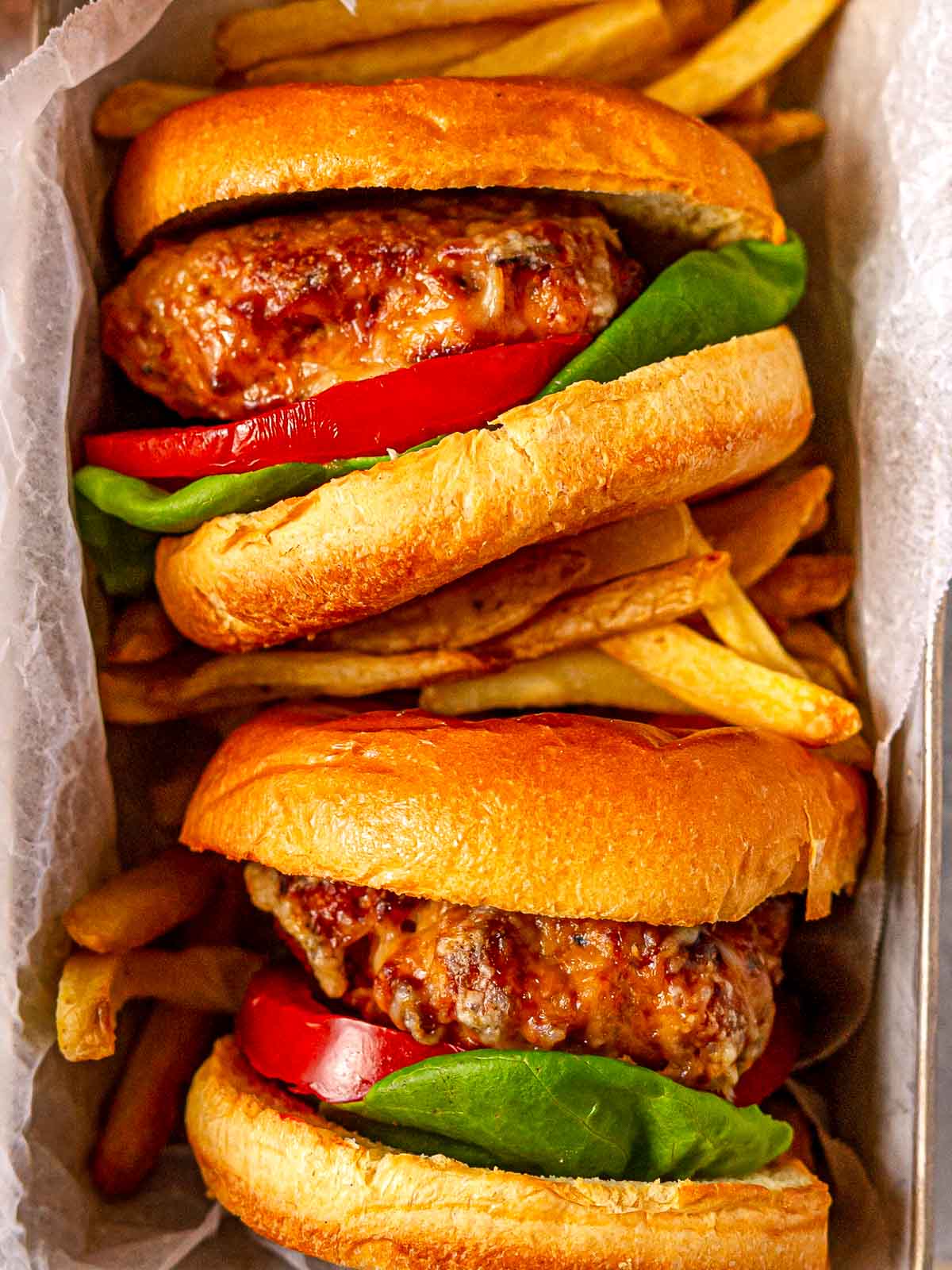Turkey burgers in a tray with golden fries, garnished with lettuce and tomato.