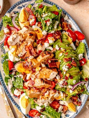 Platter of grilled chicken Cobb salad with avocado, hard-boiled eggs, tomatoes, bacon, feta, and romaine.